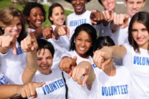 portrait of a happy and diverse volunteer group pointing towards camera