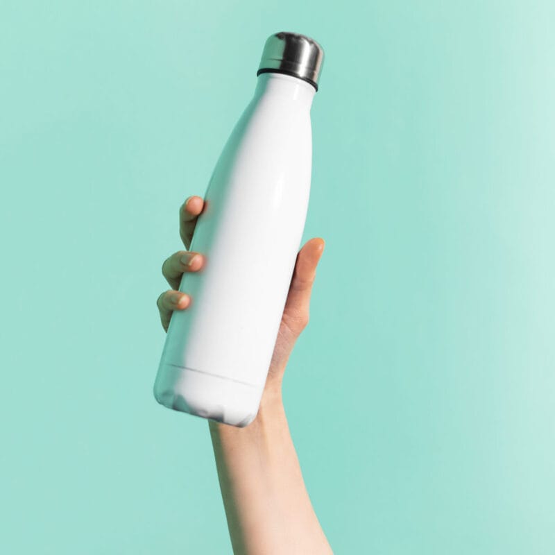 Close-up of female hand holding white reusable steel stainless thermo water bottle isolated on background of cyan, aqua menthe color. Plastic free.