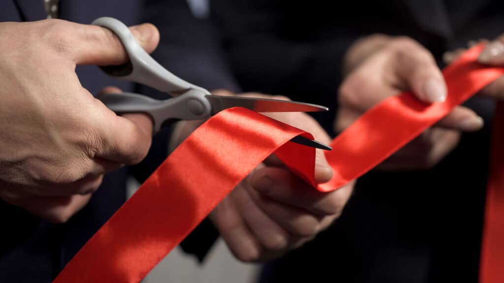 A man cutting a red ribbon with scissors
